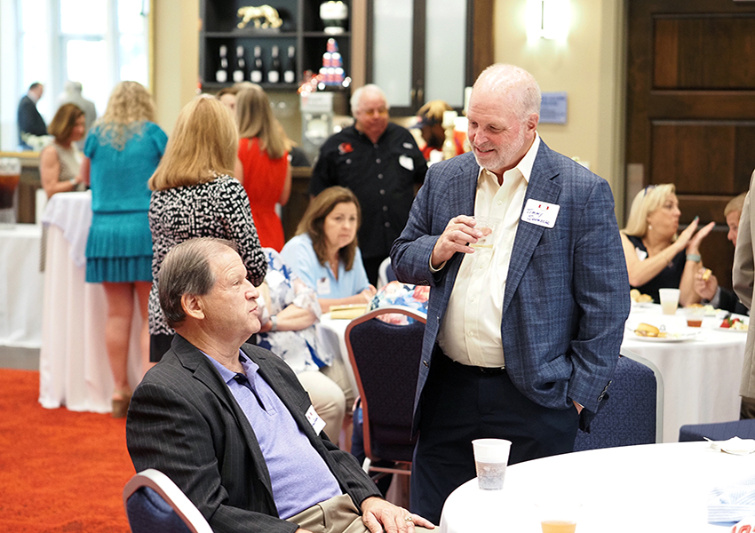 Man standing and speaking to another man sitting at a table.