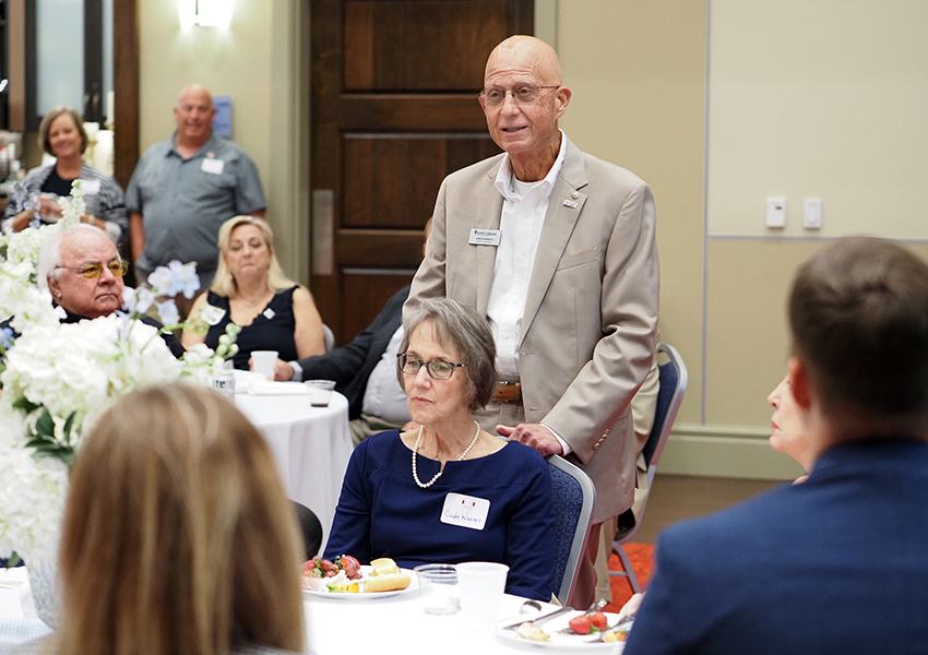 Man standing behind chair speaking at event.