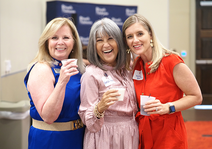 Karen Edwards with two alumni smiling all wearing dresses.