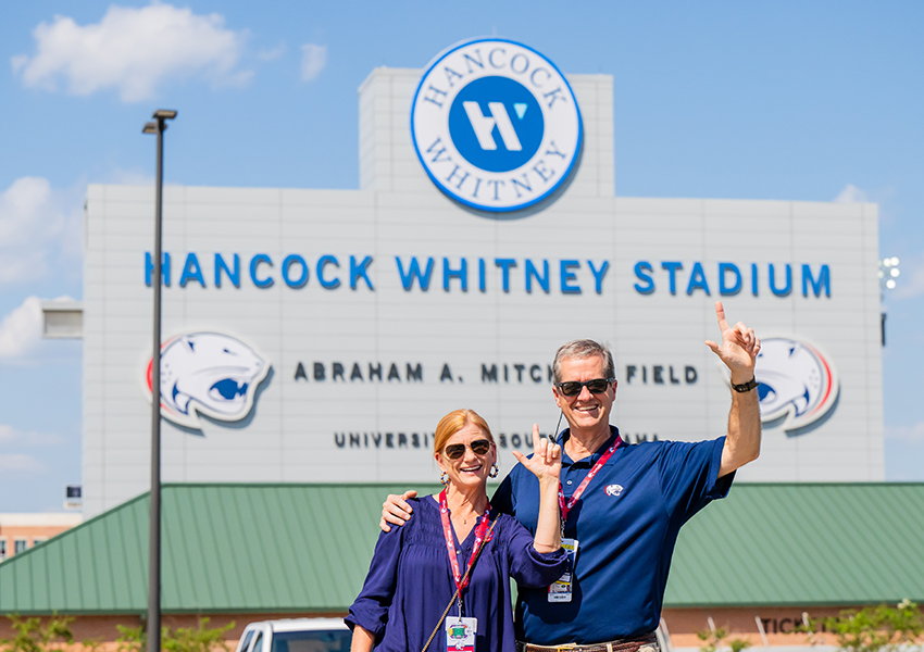 Two alumni smiling in front of Hancock Whitney Stadium.