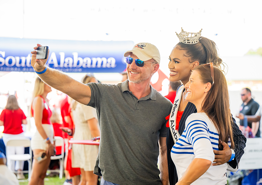 Two alumni taking a picture with Mrs. Alabama. 