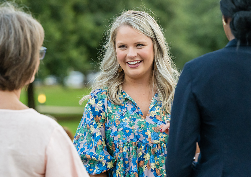 Woman smiling in floral dress talking to two people.