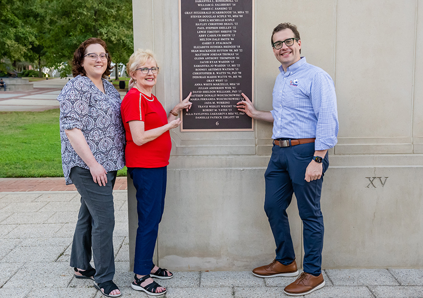 Three people pointing to the Wall of Honor.