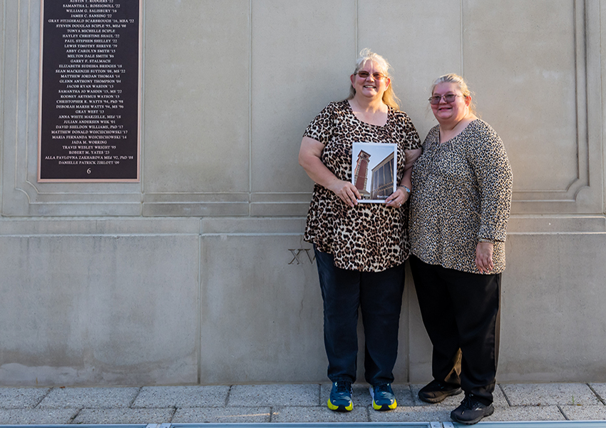 Two women in jaguar print shirts in front of Wall of Honor.