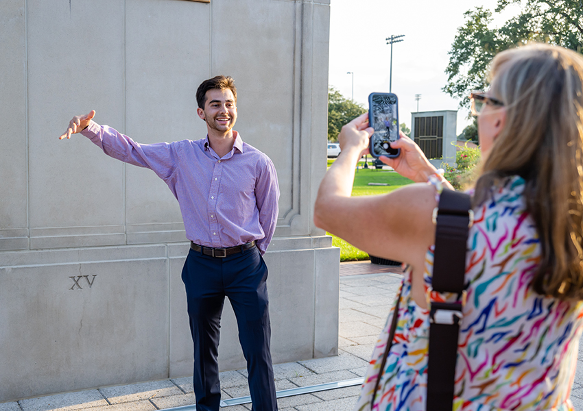 Man holding out arm in front of Wall of Honor.