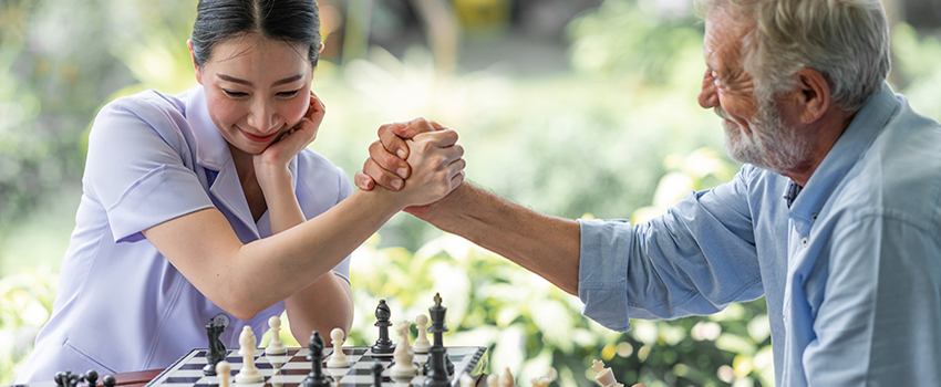 Elderly man and younger woman shaking hands after chess match.