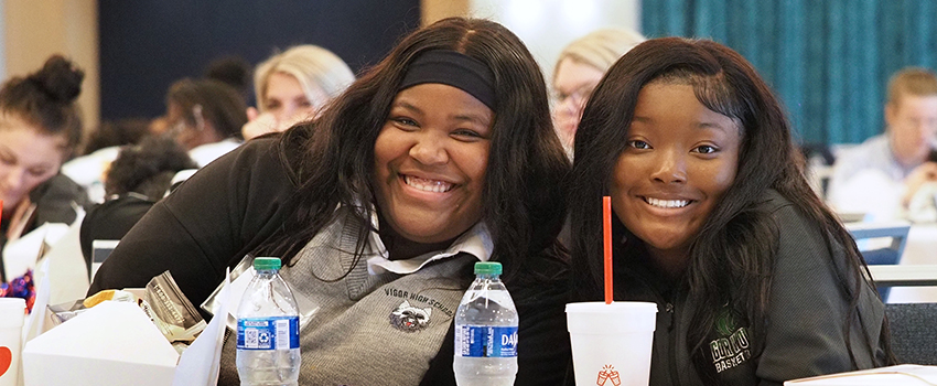 Two students smiling sitting at table.