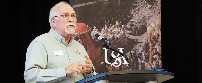 Speaker at conference talking to crowd at podium with picture behind hjm.