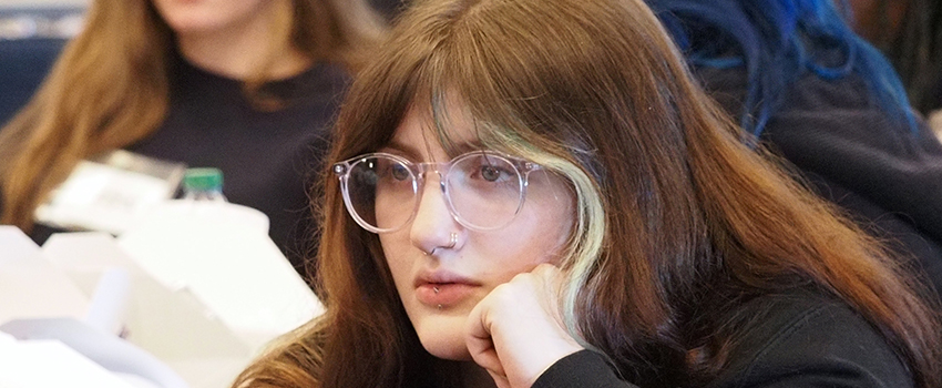 Student in glasses with hand under her chin at conference.