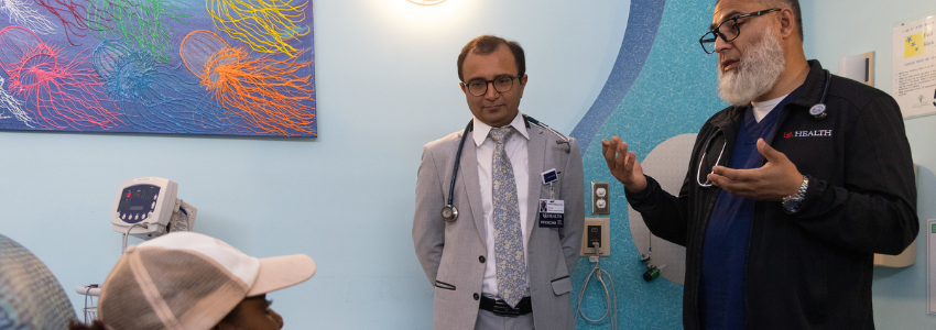 Two physicians speak with a female pediatric patient receiving treatment.