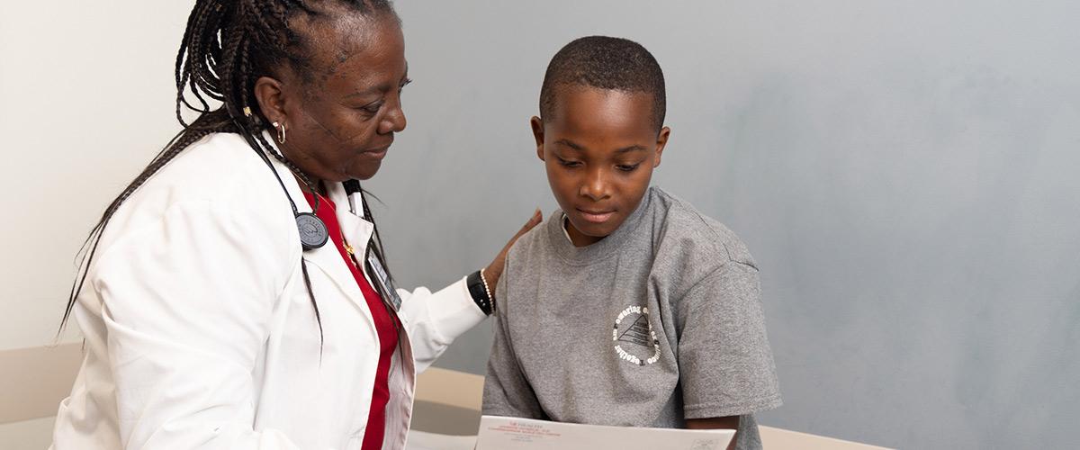 USA health doctor with pediatric patient sitting on exam table. The doctor is showing patient a document with a hand on their shoulder.