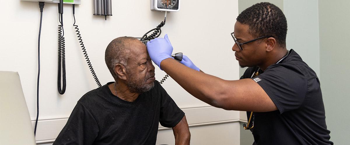 Health Physician working with elderly patient using an otoscope.