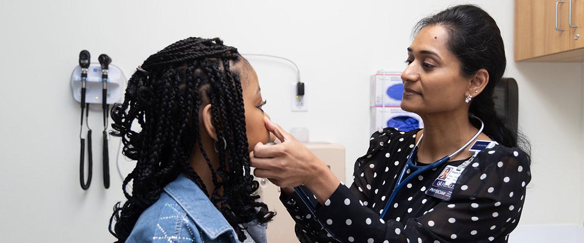 USA Health Physician working with a young woman, checking around her nose and eyes. In a doctors office.