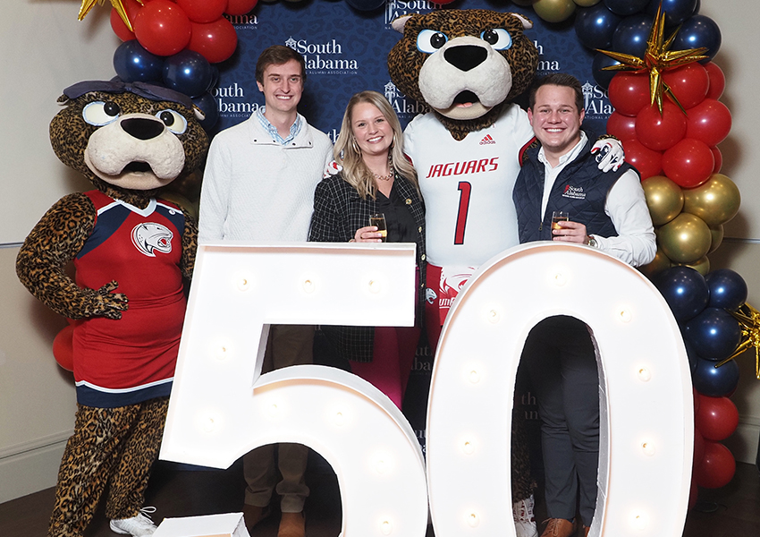 Alumni's pose behind the "50" beside Ms. Paula and South Paw