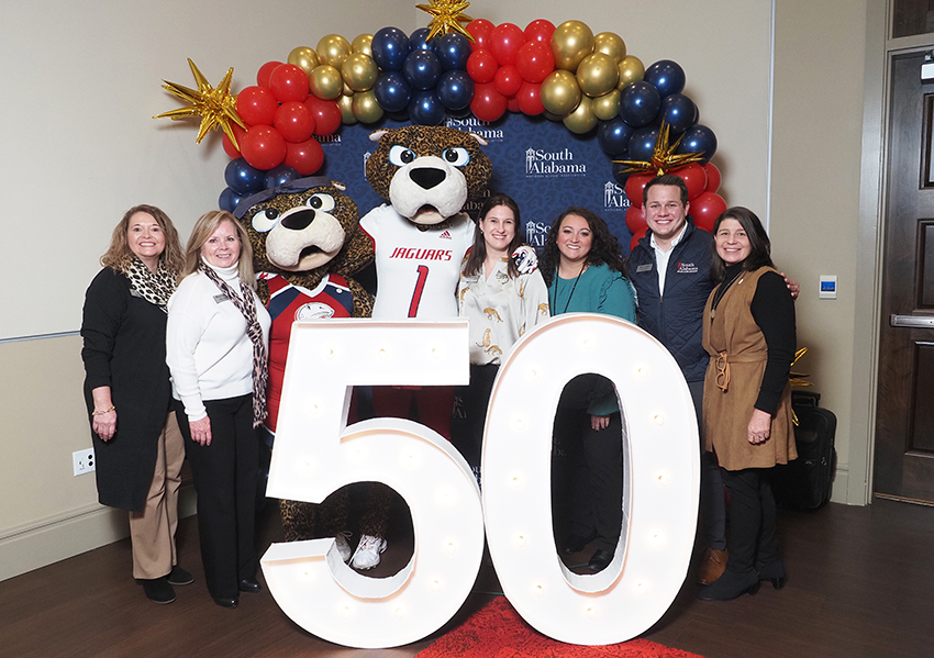 Alumni's pose behind the "50" beside Ms. Paula and South Paw