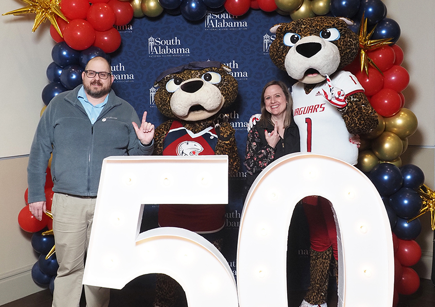 Alumni's pose behind the "50" beside Ms. Paula and South Paw