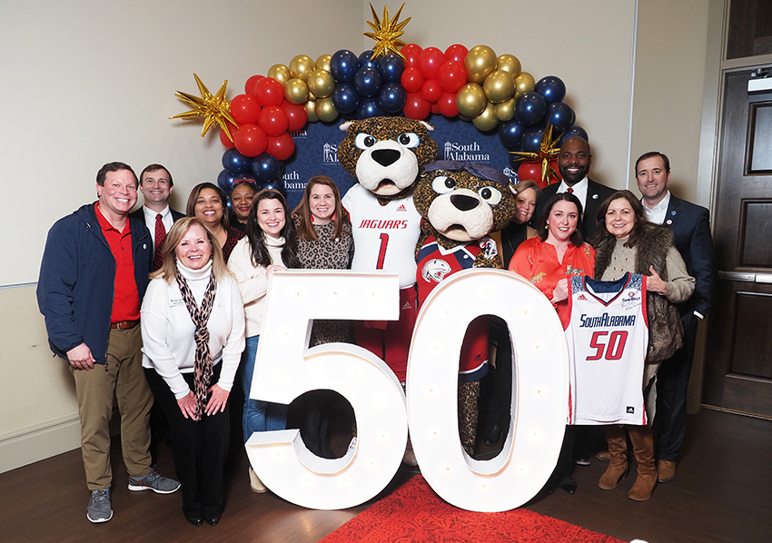 Alumni's pose behind the "50" beside Ms. Paula and South Paw