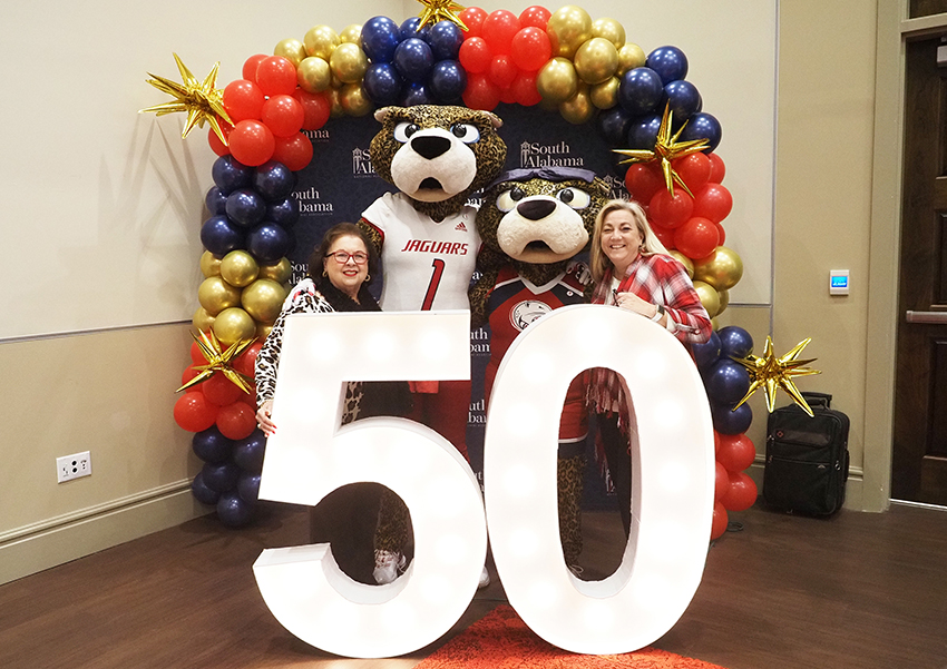 Alumni's pose behind the "50" beside Ms. Paula and South Paw