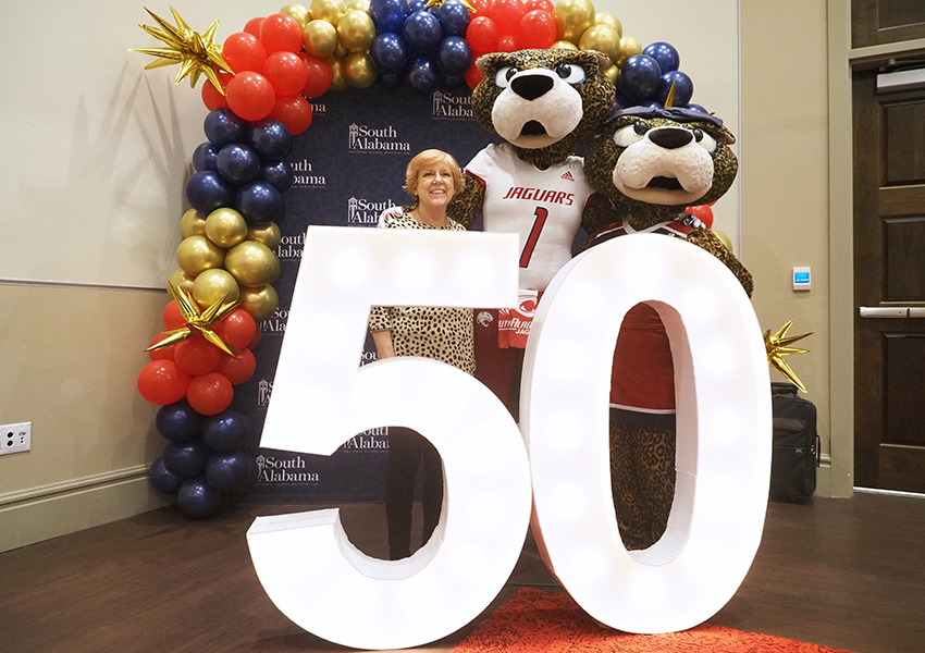 Alumni poses behind the "50" beside Ms. Paula and South Paw