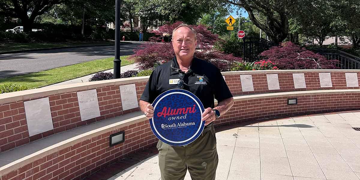Owner of Kinney Cleaning holding up Alumni owned sign