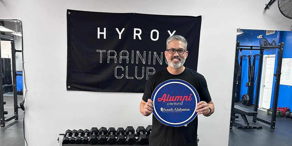 Centerline Fitness owner holding up Alumni owned sign