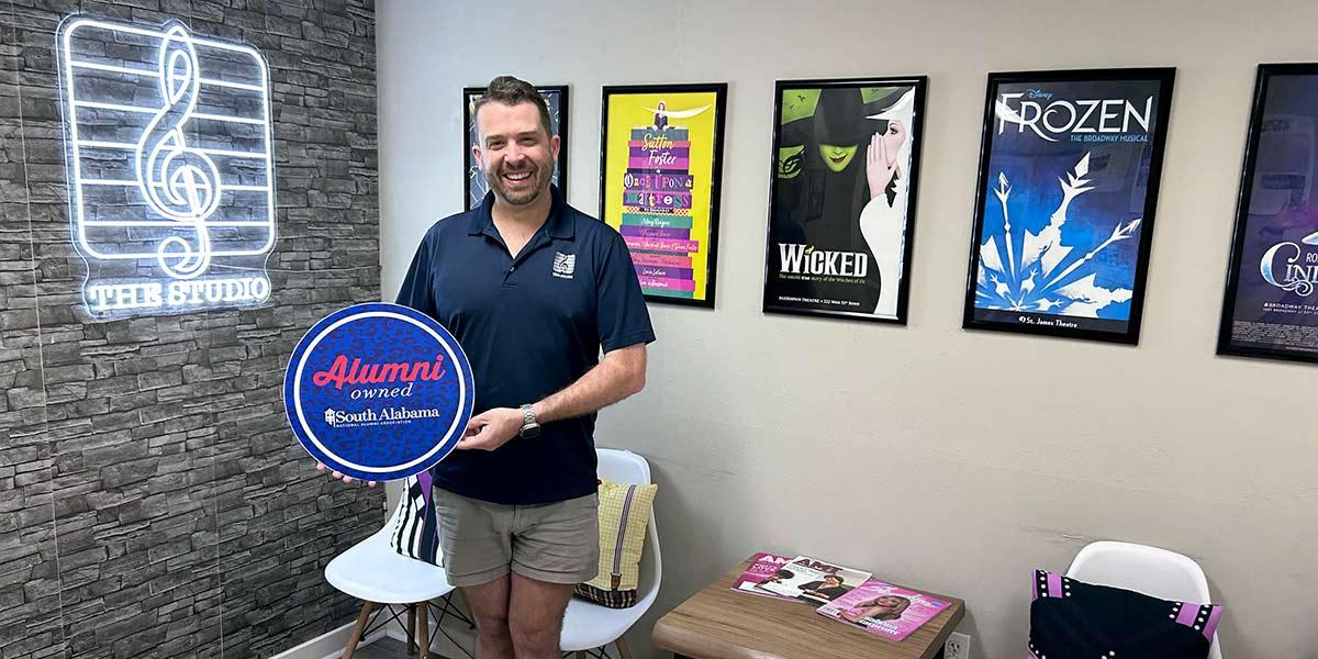 The Studio owner holding up Alumni owned sign