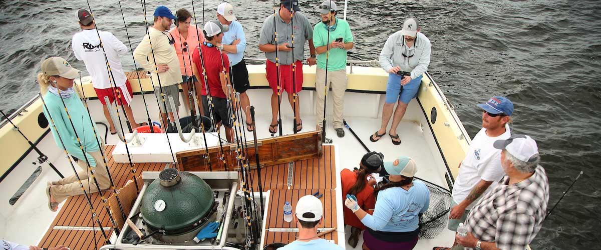 A group of marine science students on a boat with fishing rods.
