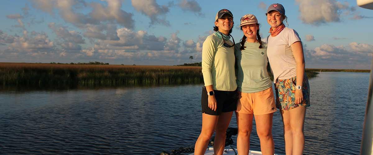 Three marine science students standing on boat over the water.