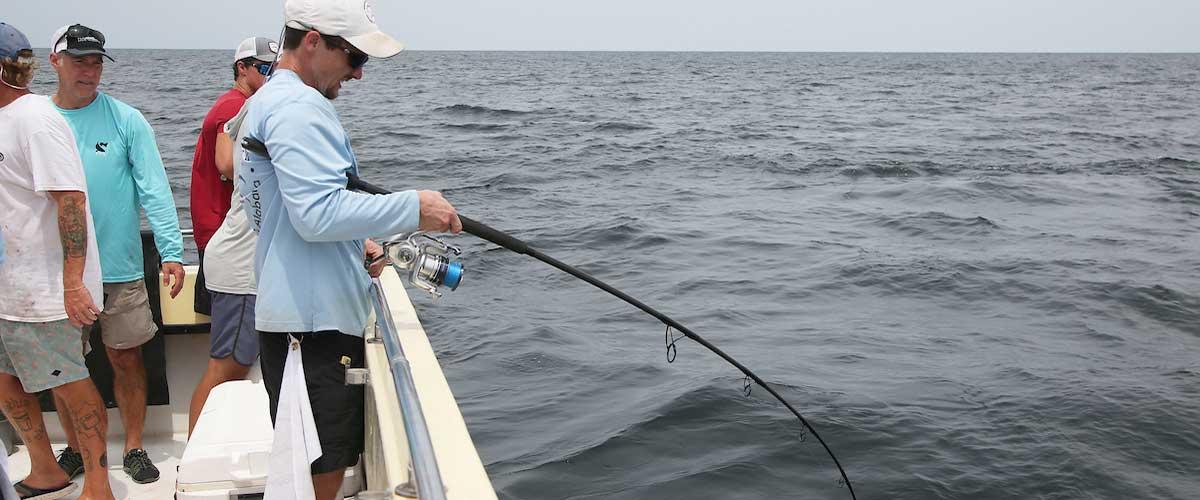 Marine science student fishing with fishing rod bent into the water.