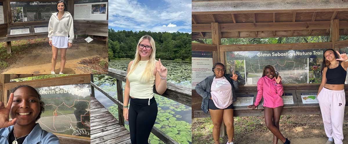 South Alabama students posing in front of the entrance to South Trails located on campus.