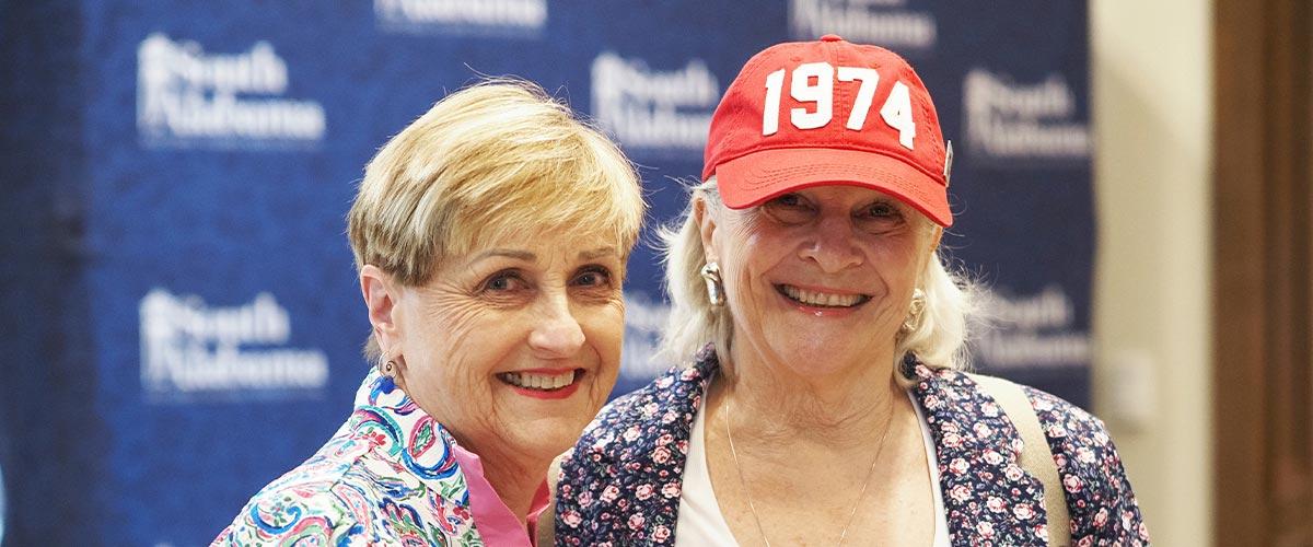 Two alumni with one wearing a 1974 hat.