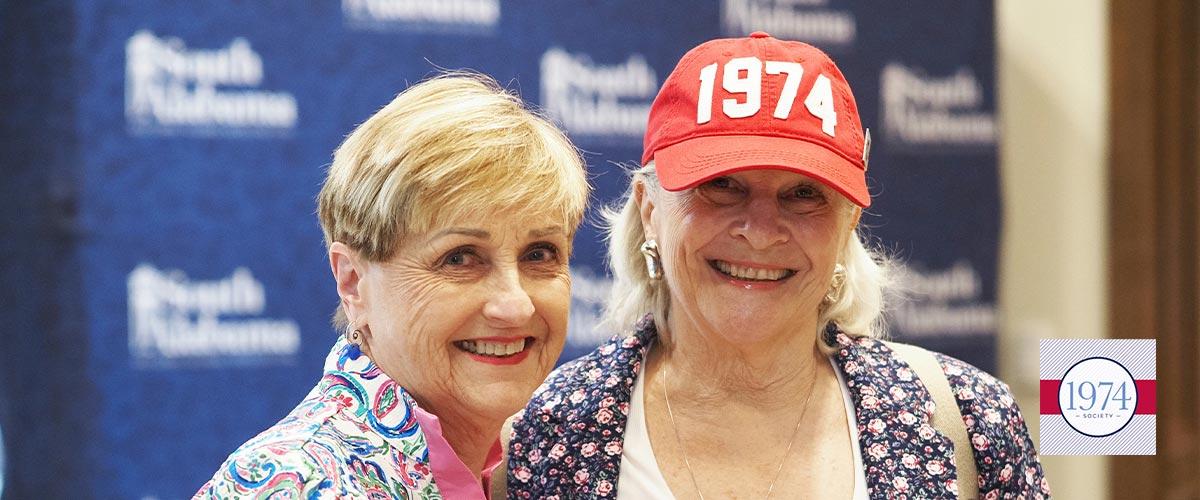 Two alumni with one wearing a 1974 hat.