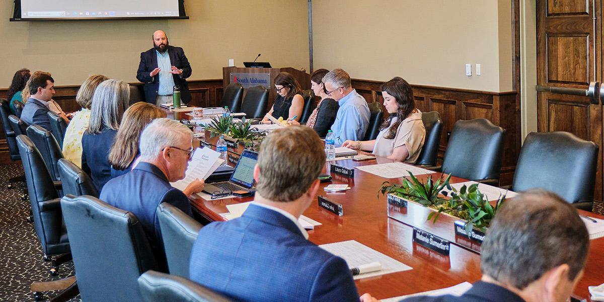 Group sitting at boardroom table while person is speaking.