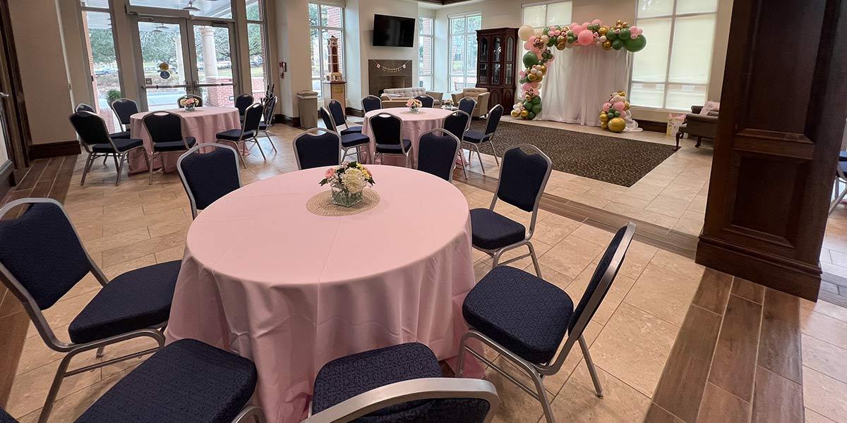 Room with tables set with pink table cloths and balloon arch photo area 