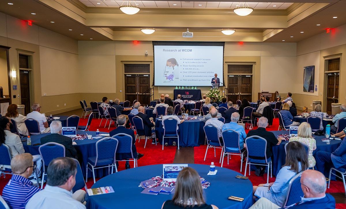 People at event in ballroom sitting at table and chairs.