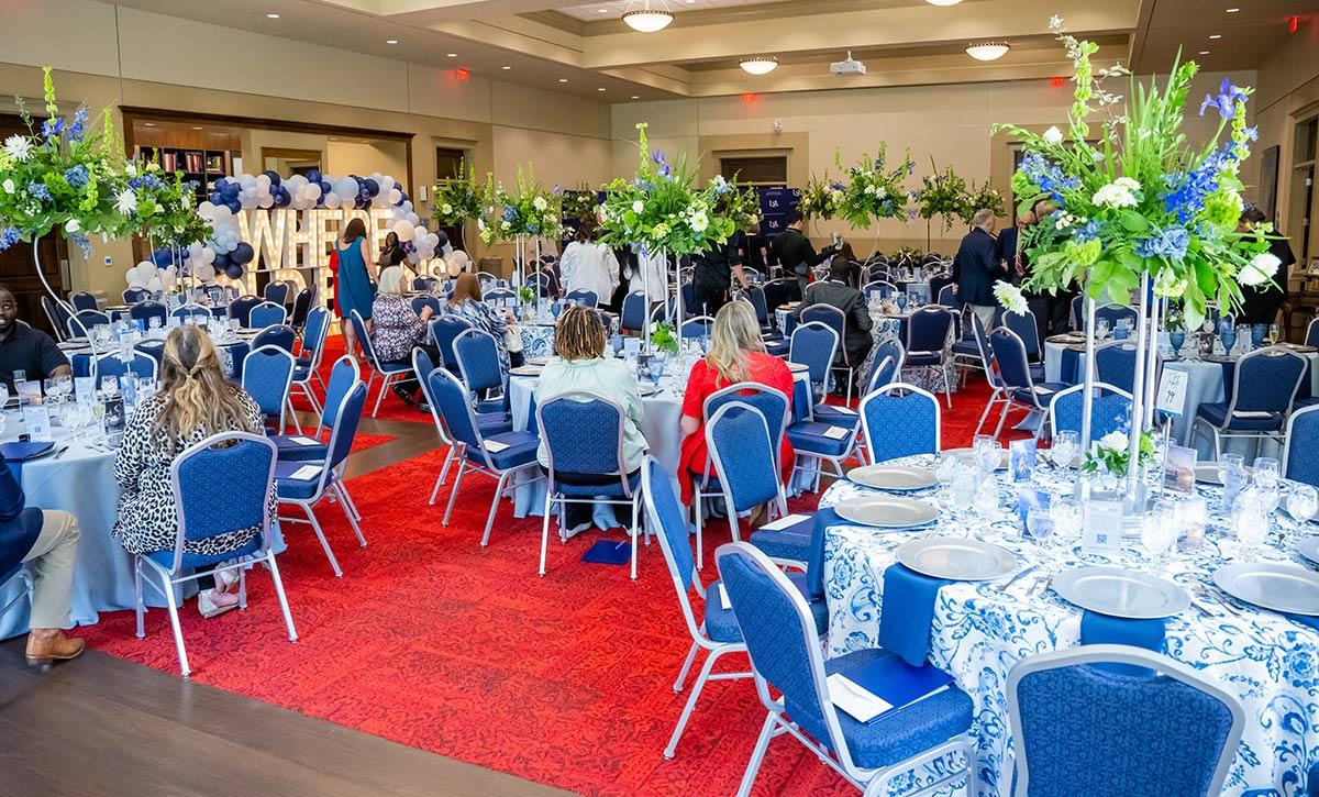Table and chairs in ballroom with flower arrangements.