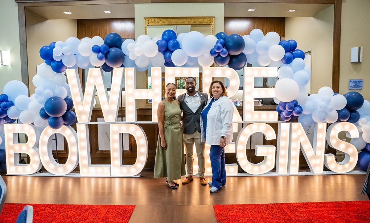 Three people in front of Where Bold Begins letter sign