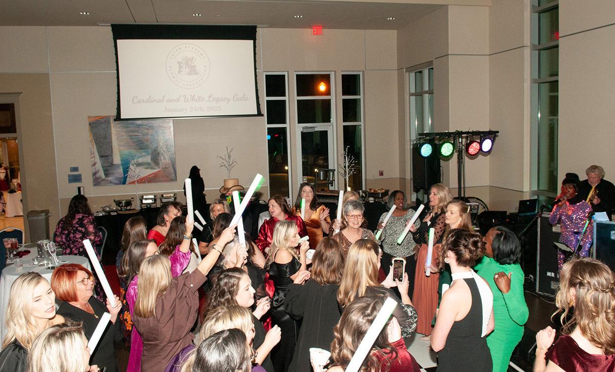 People holding glow sticks during event in ballroom.