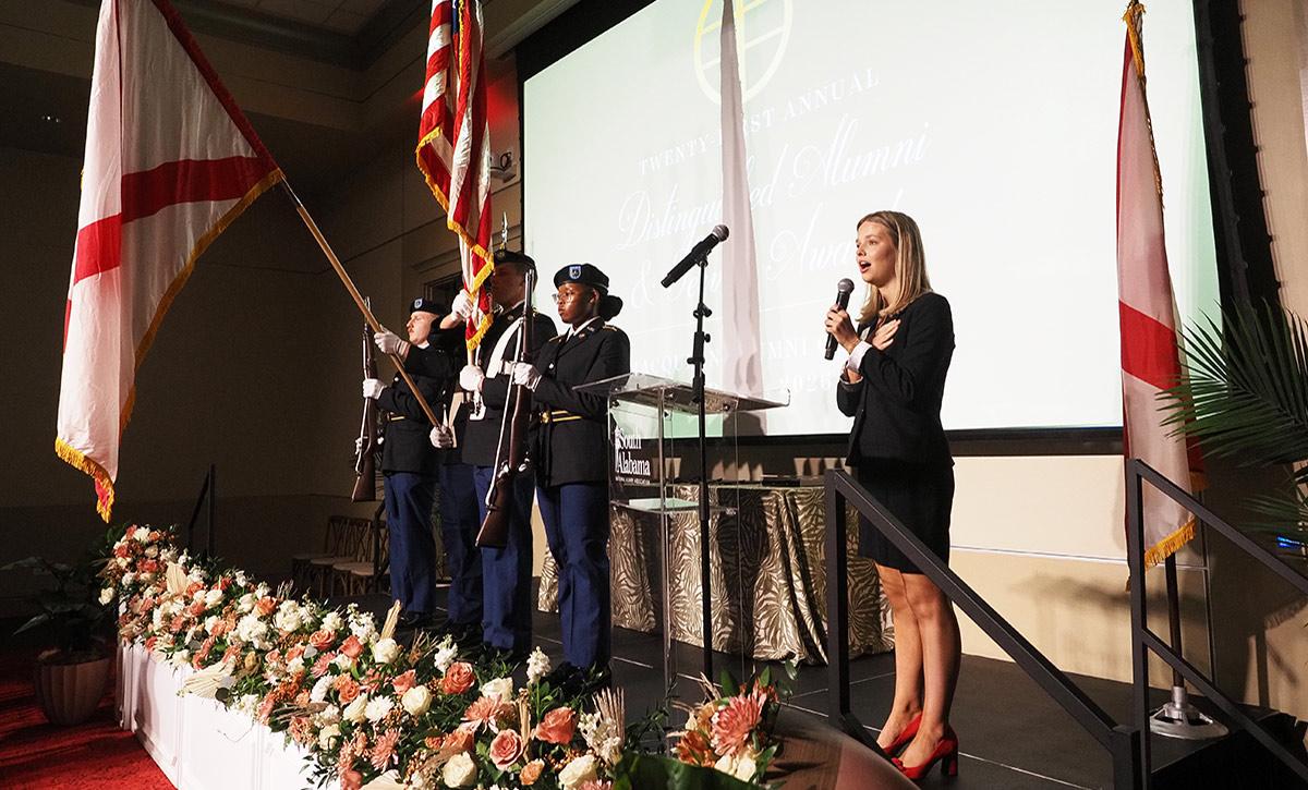 Southerner on stage speaking with military holding flags.
