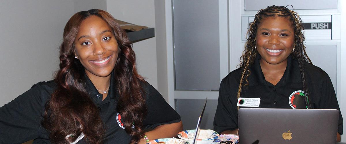 Two members smiling at table with laptop.