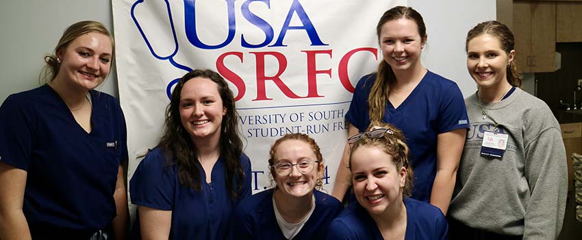 Audiology students pose with the USA SRFC banner after conducting an audiology and balancing screening at the clinic. 