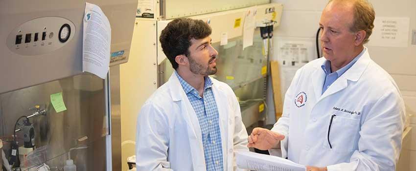 Robert A. Barrington, Ph.D speaking with another man in white coats in lab.