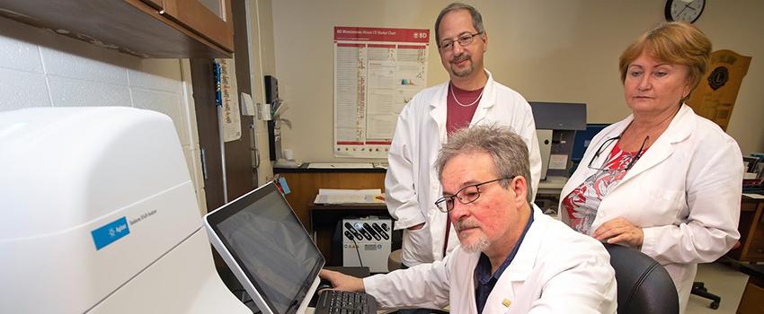 Mikhail Alexeyev, Ph.D., professor of physiology and cell biology at the USA College of Medicine, places a sample in the Seahorse XFe24 extracellular flux analyzer as Domenic Spadafora, Ph.D., manager of the flow cytometry facility at the USA College of Medicine, and research technician Nataliya Kozhukhar look on.