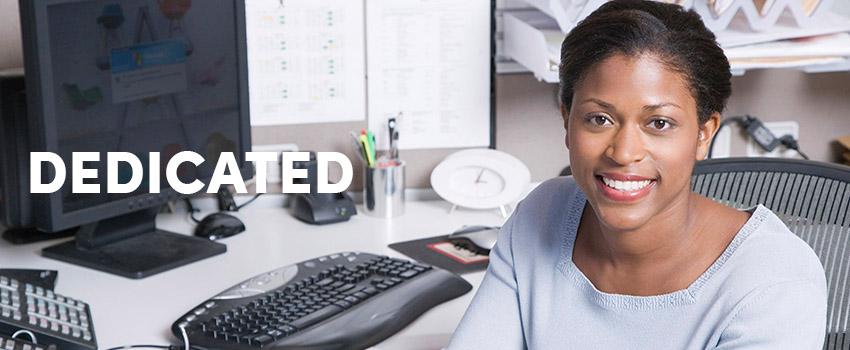 Dedicated text over woman smiling sitting at desk with computer on it.