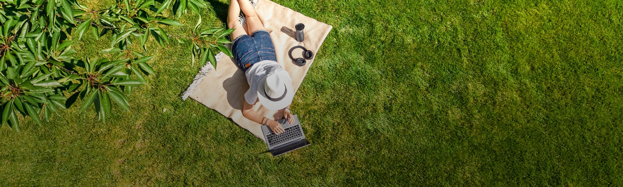 woman in a hat on a blanket outside with a laptop