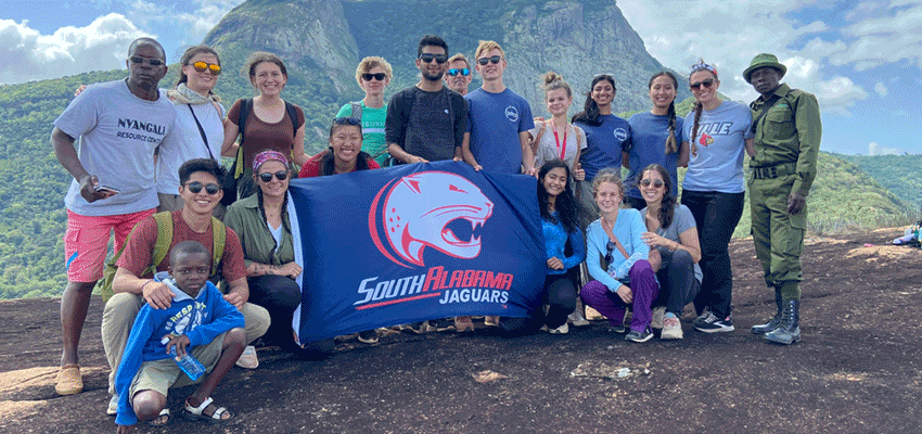 Biomedical students studying abroad in Kenya holding the Jag flag with people from Kenya.