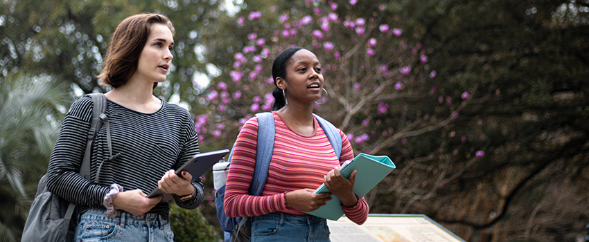 Two female students holding books walking on campus together.