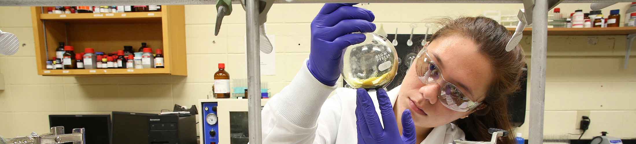 Student working in lab holding beaker.