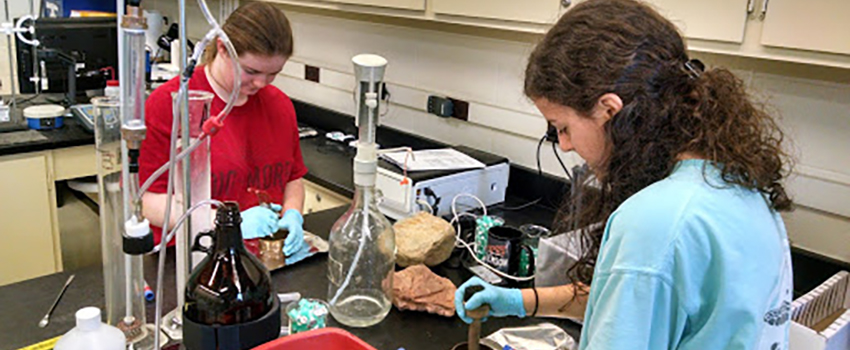 Two female students working in a lab with rocks on the table.