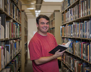 Male student in library holding a book.